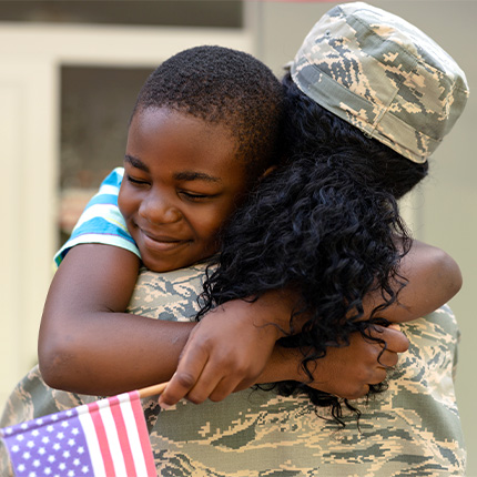 son hugging his military mom with a flag in his hand