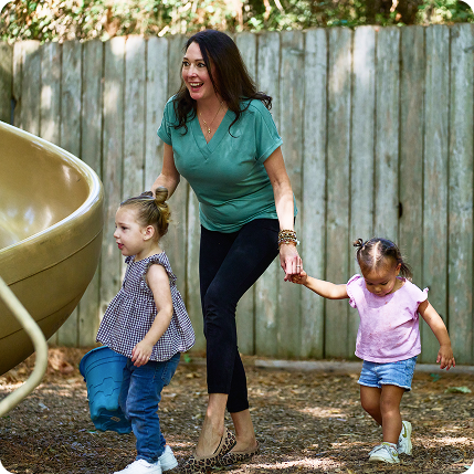 Teacher holding hands with two children outside