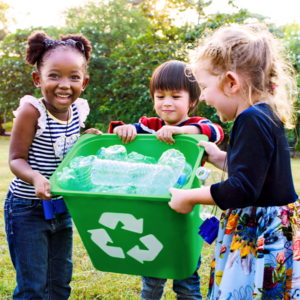 Kids outside holding green recycle bin of plastic bottles