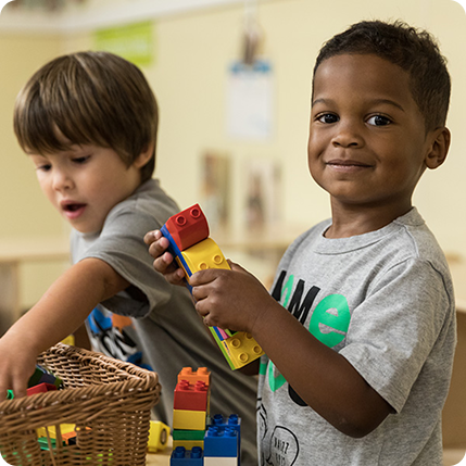 Two boys are preschool table building legos