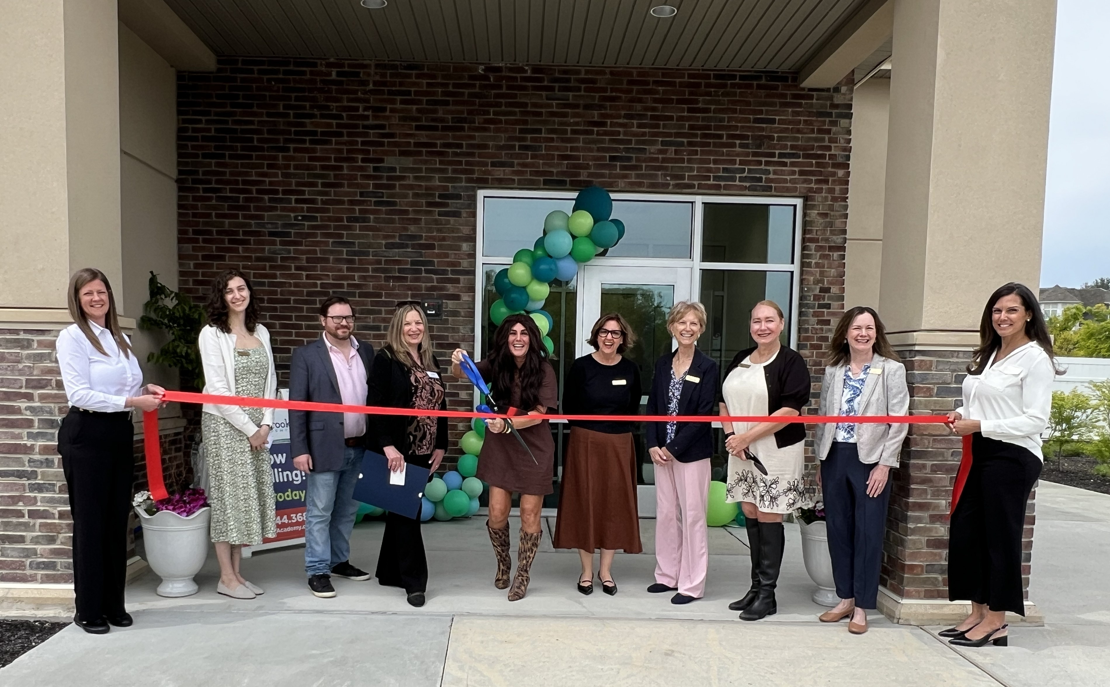 Staff standing outside school doing a ribbon cutting with large scissors